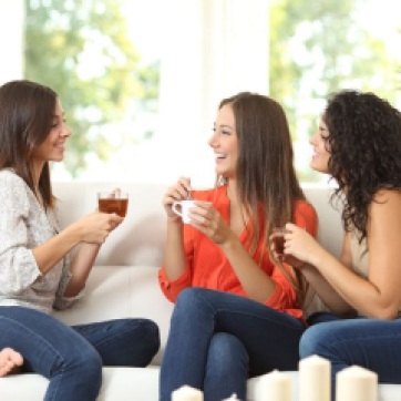 50564338 - three happy friends talking and drinking coffee and tea sitting on a couch at home